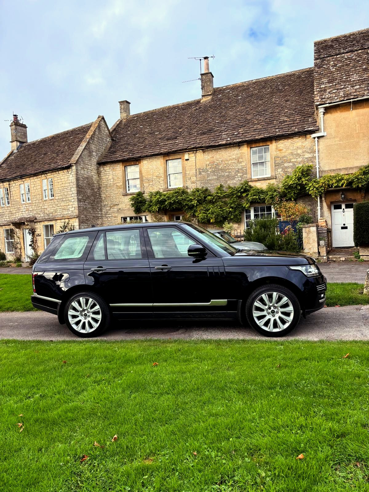 A Range Rover parked on the verge of a lane, a row of stone cottages behind it.